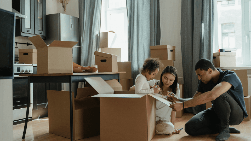 Man, woman and girl writing on box in kitchen full of moving boxes