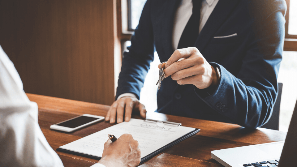 Man is passing keys while other man is signing paper